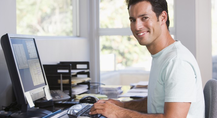 Man in home office using computer and smiling