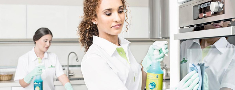 Mulher, vestida de forma profissional com avental e luvas para fazer uma limpeza de casa de forma profissional, através de serviços de franquias