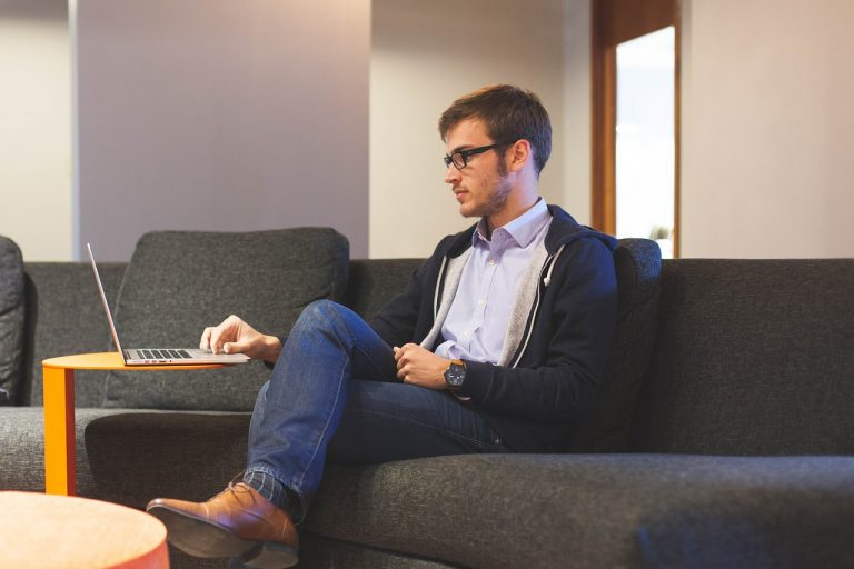 Homem jovem sentado em um sofá, mexendo no computador, representando um jovem empreendedor