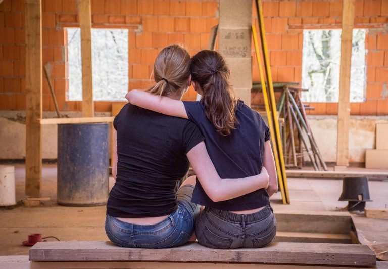 duas mulheres jovens abraçadas diante de uma sala em construção, representando cooperação