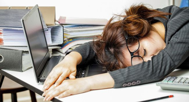 Mulher jovem dormindo em cima do teclado do computador, representando a procrastinação no trabalho