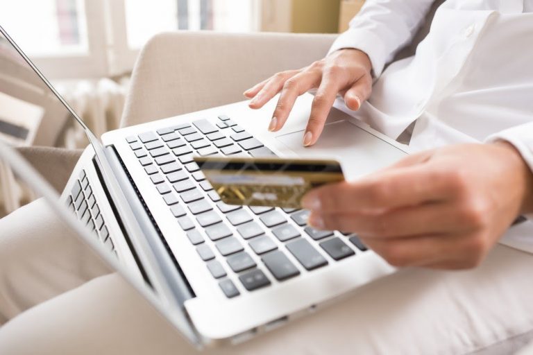 Mão em um teclado de computador e a outra segurando um cartão de crédito, representando o e-commerce